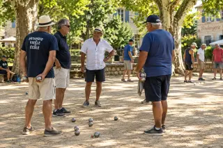 Group of pétanque players chatting on a shaded Provençal boulodrome with metallic boules and a cochonnet scattered on the sunlit ground